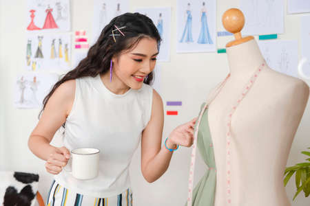 Asian tailor woman working on clothes in tailoring atelier,  beautiful young female fashion designer working tailoring new handmade dress in workshop.の写真素材