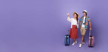 Happy couple tourist hand pointing to copy space with baggage going to travel on holidays isolated on purple background.の写真素材