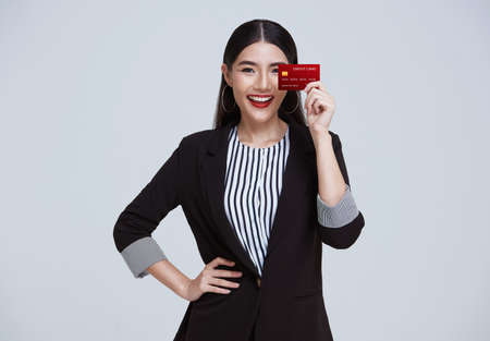 Smiling Confident Asian business woman showing credit card isolated on gray background.