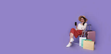 Amazed woman sitting on chair and showing mobile phone and shopping bags on purple background.の写真素材