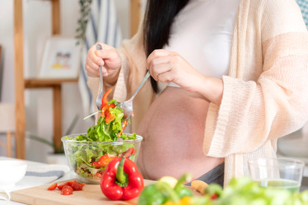 Happy asian pregnant woman cooking salad at home, doing fresh green salad, eating many different vegetables during pregnancy, healthy pregnancy concept.の写真素材
