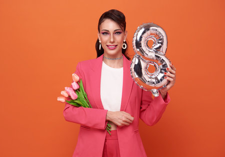 International Women's Day. Extremely happy woman in pink clothes she is holding tulip flowers and number 8 in her hands isolated on studio background.の写真素材