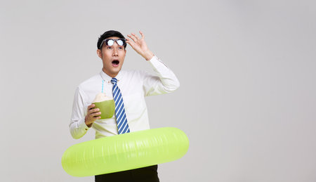 Business travel summer time. Excited asian businessman holding coconut water and swim inflatable ring isolated on white background.の写真素材