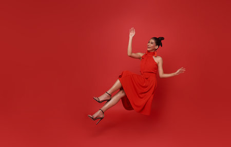 Young beautiful smiling asian woman red dress floating in mid-air relaxing isolated on red background.の写真素材