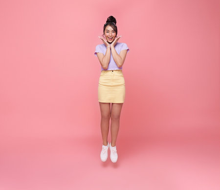 Happy Asian teen woman smiling and jumping while celebrating success isolated on pink background.の写真素材