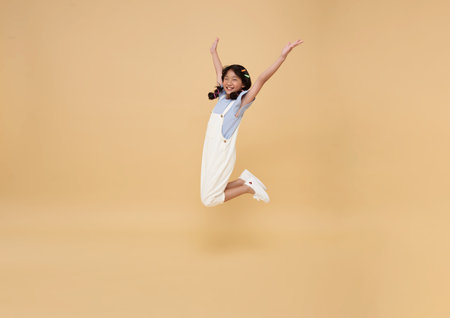 Full length cheerful Asian children kid girl jumping and raising hands up isolated on nude color background.の写真素材