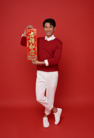 Happy Chinese new year. Asian man holding greeting couplets isolated on red background. Chinese text means May you have happiness and prosperity.の写真素材