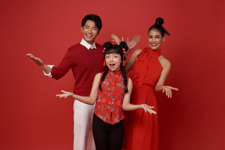 Happy asian family wearing red costume presenting or showing open hand palm with copy space for product isolated on red background. Present product advertising concept.の写真素材