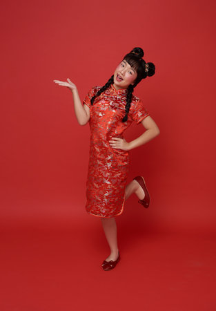 Happy smiling children asian girl in red traditional cheongsam qipao with gesture of welcome chinese new year 2024 isolated on red copy space background.の写真素材