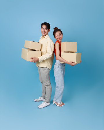Happy young family asian couple man and woman moving boxes to their new home apartment isolated on blue background.の写真素材