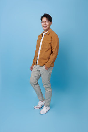 Full body smiling happy young Asian teen man walking going strolling and looking isolated on blue background studio portrait.の写真素材