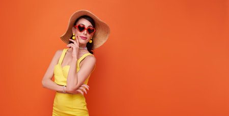 Happy young sexy fashion woman slim body wear yellow swimsuit straw wide brim hat posing isolated on orange color background studio. Summer hotel pool sea rest sun tan conceptの写真素材