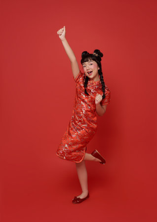 Happy Chinese new year. Asian children girl wearing traditional cheongsam qipao dress with happy hand up isolated on red background.の写真素材