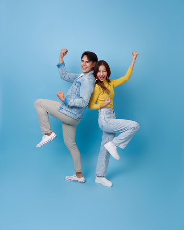 Happy Asian couple back to back doing winner gesture celebrate clenching fists say yes isolated on blue studio background.の写真素材
