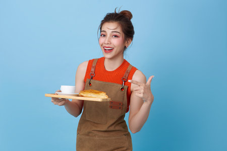 Happy barista asian woman serving customer holding coffee cup at coffee shop isolated on blue background.の写真素材