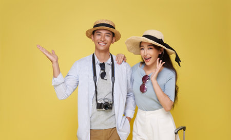 Happy Asian couple dressed in summer clothes open hand and announce welcome traveler trip isolated on yellow background.の写真素材