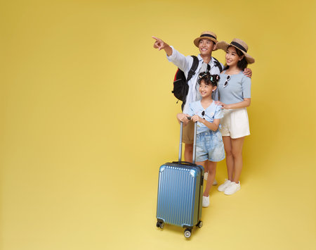 Happy fun asian family vacation portrait ready for travel with suitcase pointing finger isolated on yellow background.の写真素材