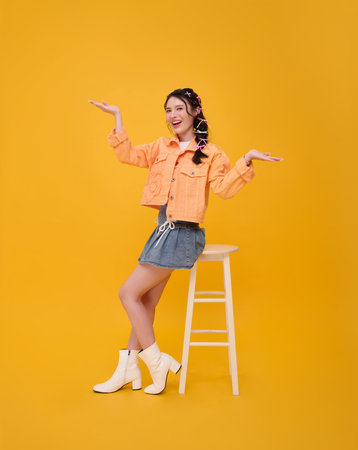 Happy beautiful young asian teen woman sitting on chair presenting or showing open hand palm with...