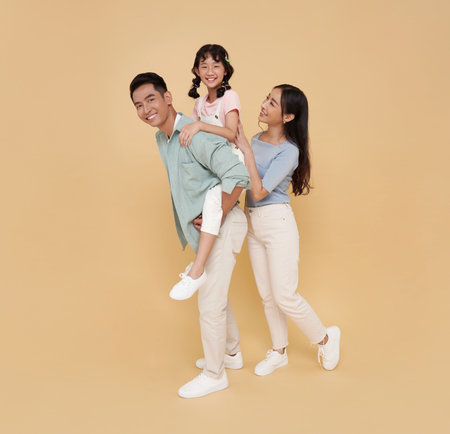Full body portrait happy asian family fun playing standing giving piggyback ride to daughter, sit on back isolated on nude color background.の写真素材