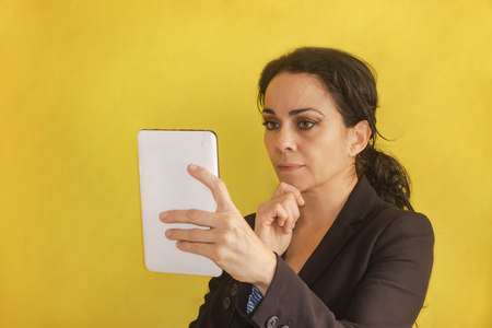 Beautiful young business woman, with pigtail, black jacket, isolated on a background, looking at her tablet. Woman analyzing dataの写真素材
