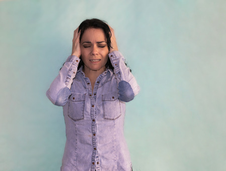 Brunette woman suffering from headache and migraine desperate with hands on her head, isolated on a...