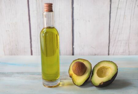 Avocado oil first cold pressing, in a glass jar, with an avocado split on light wood