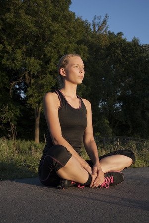 beautiful young woman is doing breathing exercises sitting cross legged after running outdoorsの写真素材