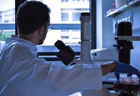 Science PhD student with glasses works tired and focused in the microscopeの写真素材