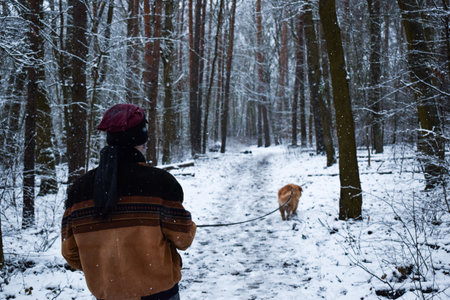 Male with his dog on a leash walking on snowy pine forest in winterの写真素材