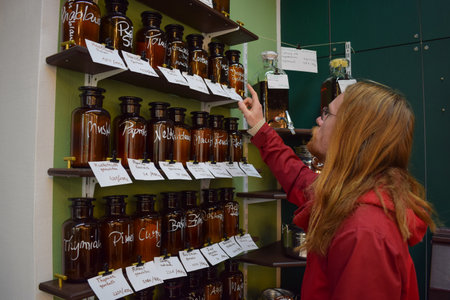 Long ginger hair caucasian hippie boy pointing at a shelf of bottles while buying organic and natural spices in a local bulk store saving moneyの写真素材