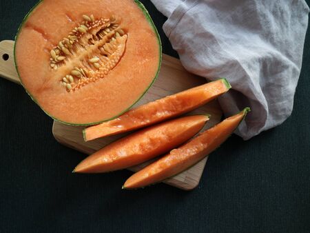Cantaloupe Orange Melon and some slices on a wooden table with a purple cloth