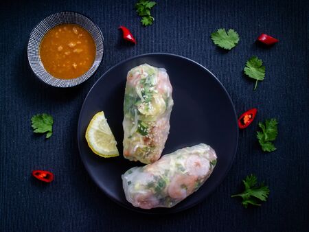 Summer rolls on a plate with lemon, coriander, peppers and dsweet and sour sauce to dip.