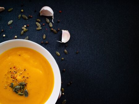 Cream made with pumpkin and carrot on backgound decorated with pepper and seedsの写真素材
