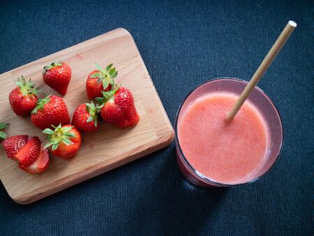 Glass with red smothie and a wooden table with some strawberriesの写真素材