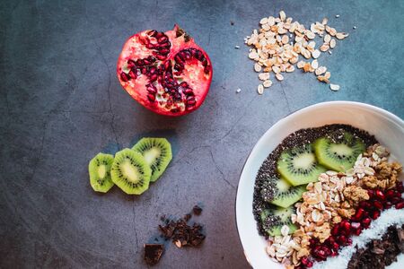 Smoothie bowl with kiwi, coconut, chia, oats, grains and pomegranate on concrete background. Top viewの写真素材
