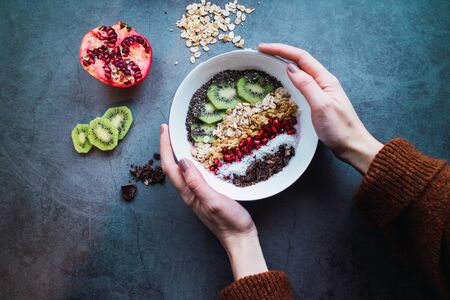 Woman's hands holding a smoothie bowl with vegan ingredients on concrete background. Healthy life Flat lay.の写真素材