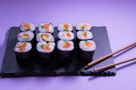 Salmon and avocado maki rolls with chopsticks on a slate plate. Japanese cuisine.の写真素材
