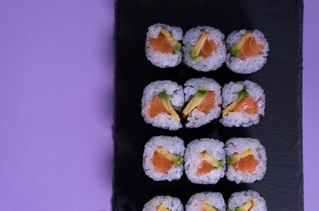 Maki sushi set with salmon and avocado on a slate plate and purple background. Japanese cuisine....