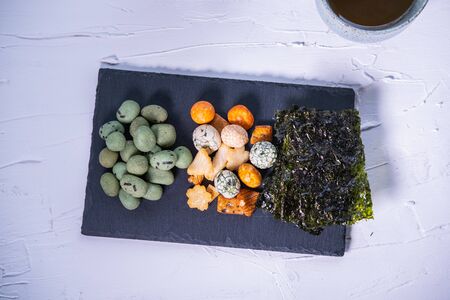 Wasabi peanuts, Japanese crackers and Korean seaweed chips on a slate plate on white background....