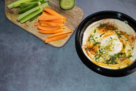 Hummus with olive oil, paprika, tahini and parsley on a black plate and some pieces of carrot and...