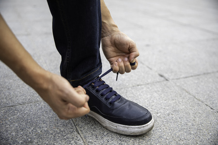 Hands of young man tying shoe laces in the street