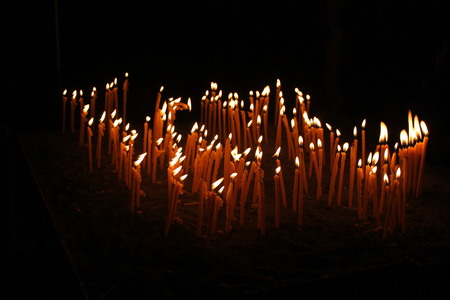 Thin candles lightening in the darkness, spiritual glowing in monastery, composition of candlesの写真素材