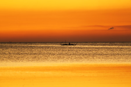 Small boat with fisherman swim on sea. Beautiful bright yellow background of sunset. Water surface scintillates on the sunset shine.の写真素材