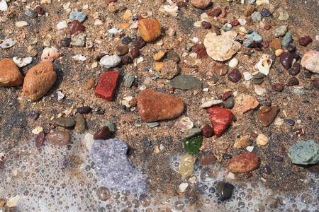 Colorful small stones on the beach with a bit of foam on the sea waterの写真素材