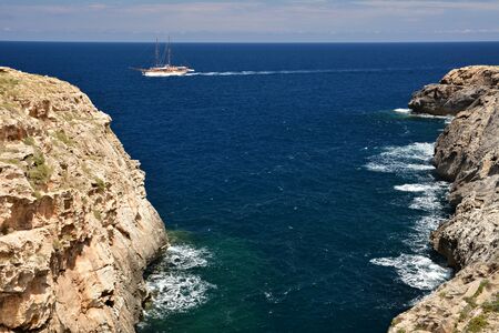 Wied il-Ghasri gorge with clean water surrounded by high clifs; sail boat on the seaの写真素材