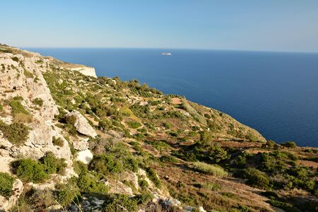 View from Dingli Cliffs on Malta. Rocky terrain with blue waters of Mediterranean Sea and small island on the horizon.の写真素材