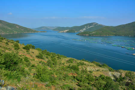 Blue waters of Koman Lake in northern Albania. Reservoir built on Drin river, surrounded by forested hills and gorges. Fishes farming on the lake.の写真素材