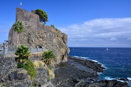 The Aci Castle on the high volcanic rock on the seaside with cliffs and blue waters aroundの写真素材