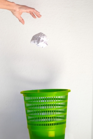 Hand going garbage in green plastic trash bin from paper isolated on whiteの写真素材