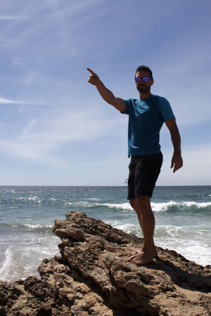 Guy on a rock on the beach pointingの写真素材